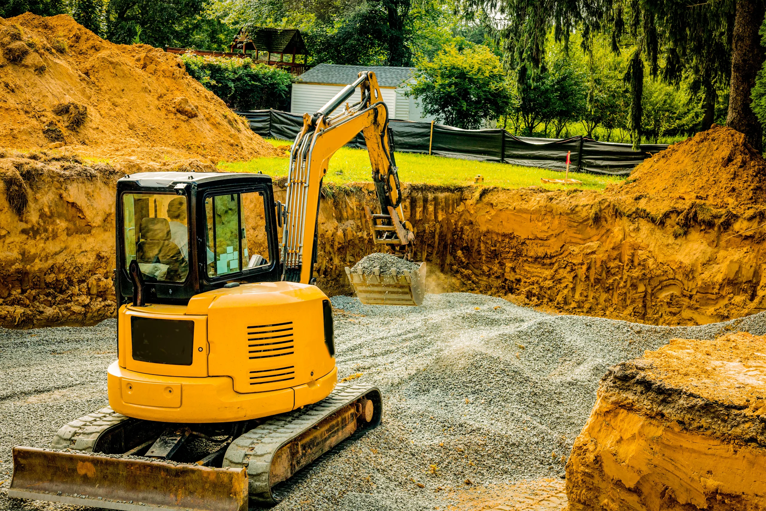Mini excavator spreading gravel in a residential foundation excavation